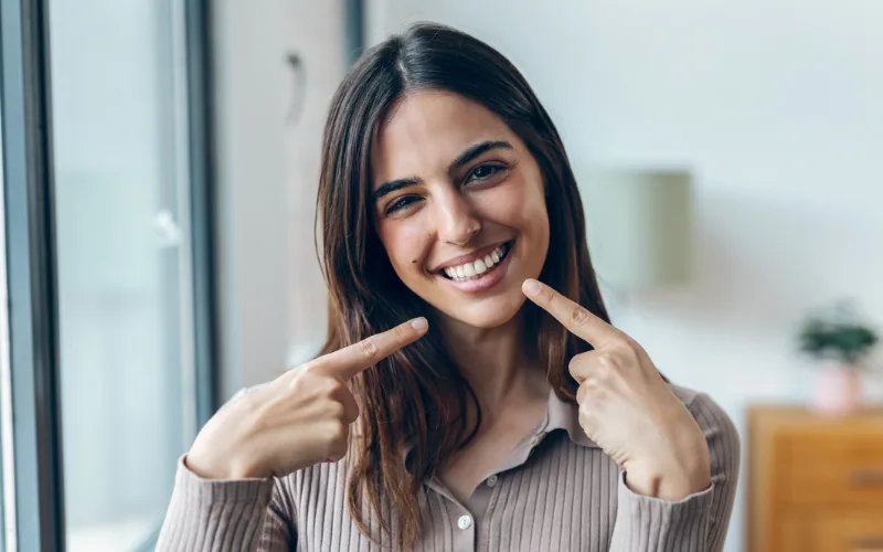 Mujer sonriente señala sus labios con los dedos índices