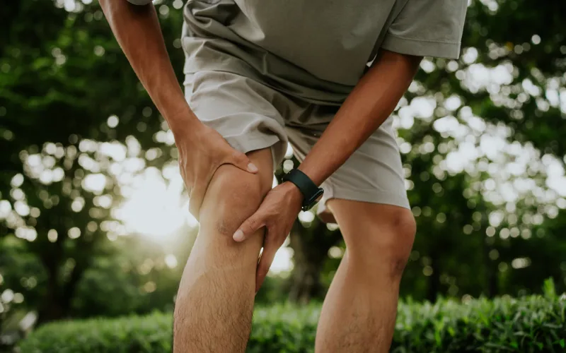 Hombre al aire libre se sujeta la rodilla con ambas manos