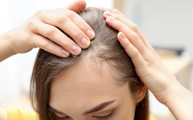 Mujer joven se separa el cabello y muestra las primeras canas
