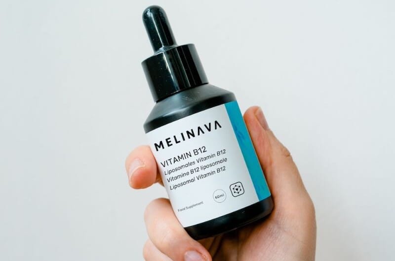 Mano sostiene un frasco con cuentagotas de vitamina B12 liposomal de MELINAVA