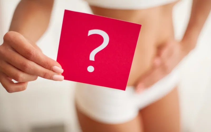 Mujer sostiene una tarjeta roja con un signo de interrogación frente al abdomen