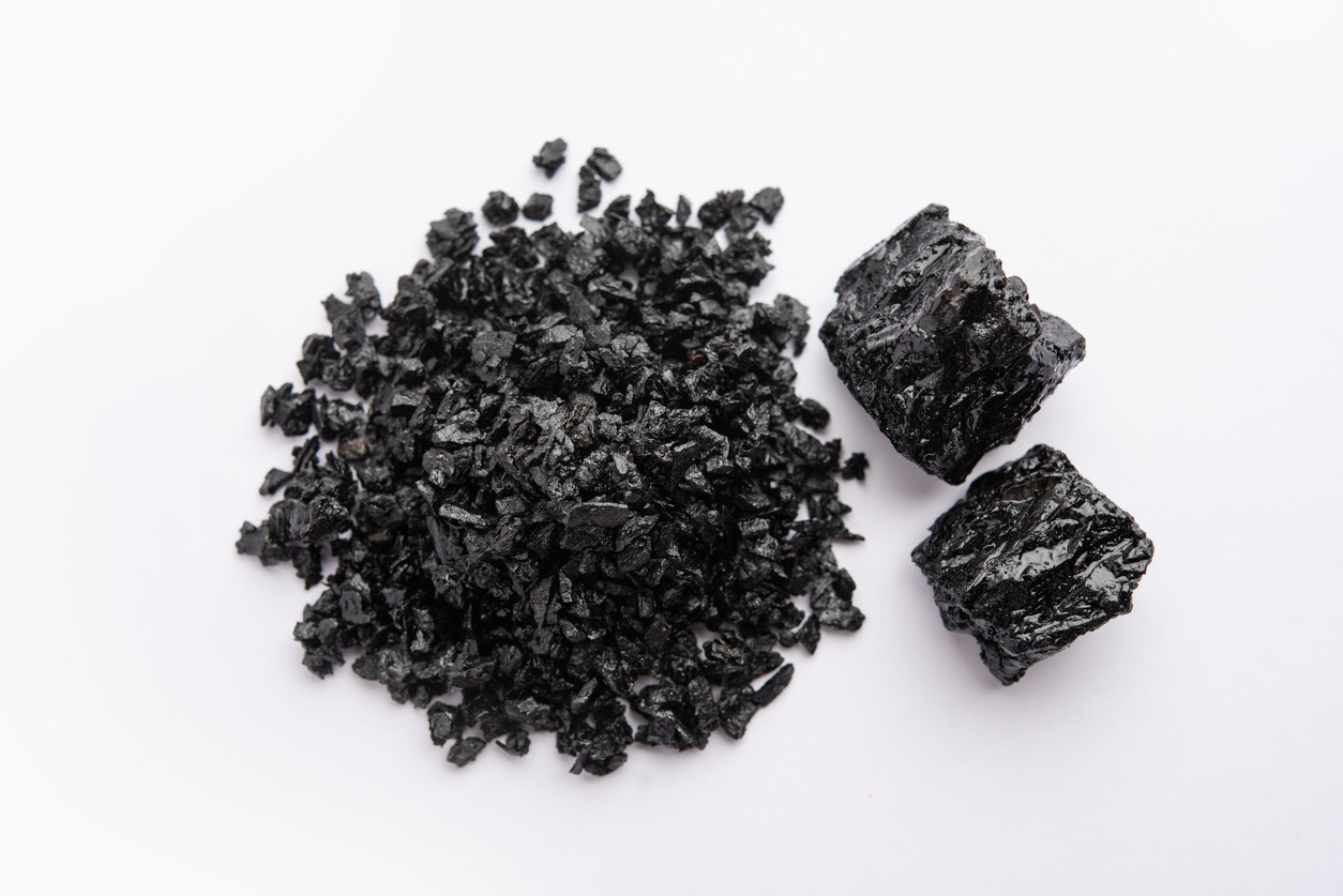 Resina de shilajit en bruto, en trozos y en granulado, sobre un fondo blanco